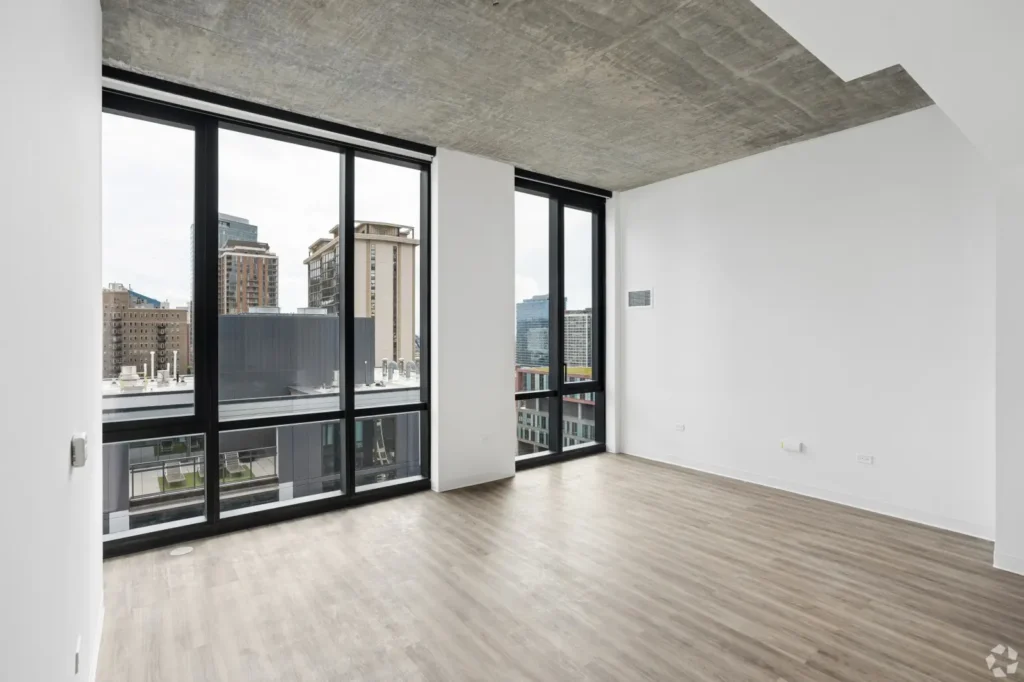 Open living and dining room with a sectional sofa, round dining table, TV, and floor-to-ceiling windows.