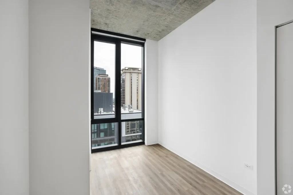 Primary bedroom with a blue upholstered bed, lounge chairs, and floor-to-ceiling windows overlooking Chicago.