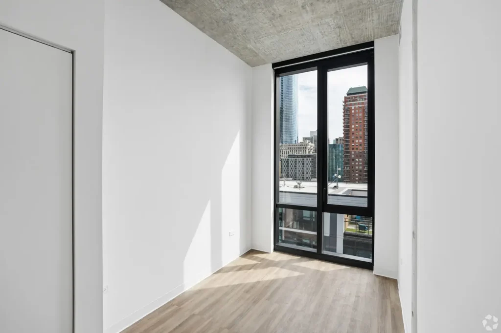 Second bedroom with an upholstered bed, nightstand, wall-mounted TV, and Chicago skyline views.