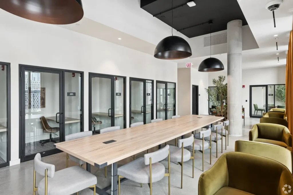 Coworking space with communal wood tables, desk chairs, pendant lights, and lounge seating.