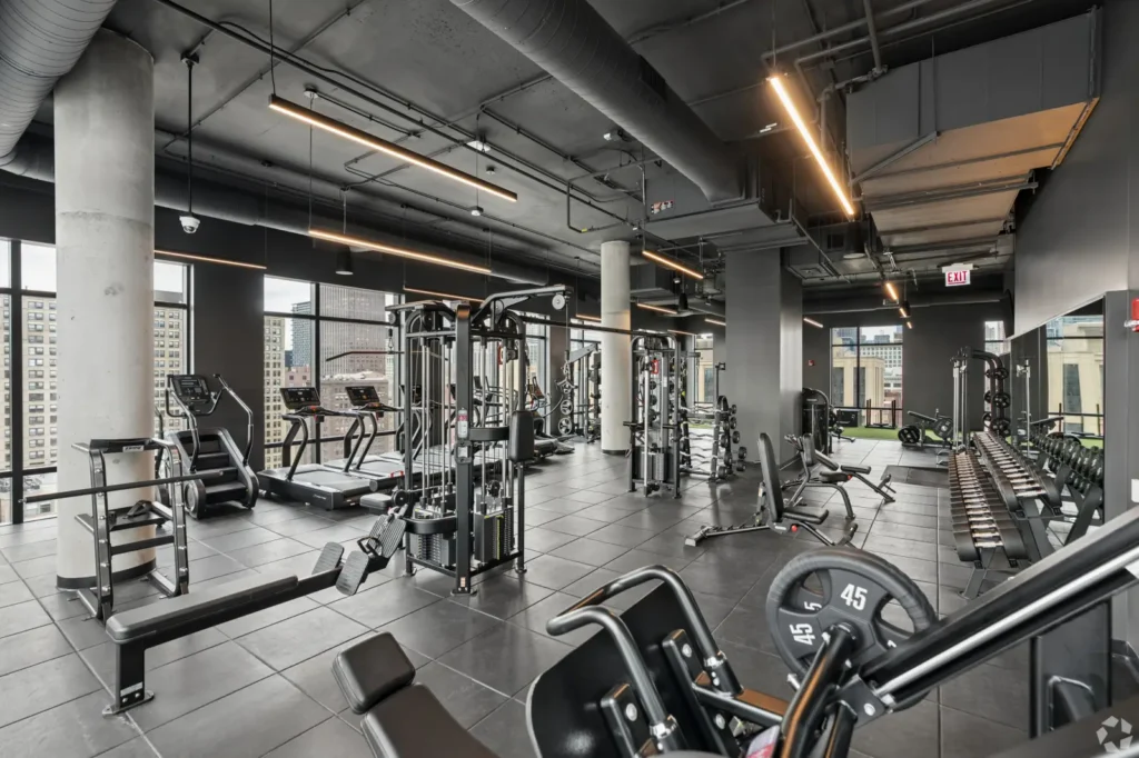 Fitness center with stair-climbing machines, strength equipment, mirrors, and wall-mounted TVs.