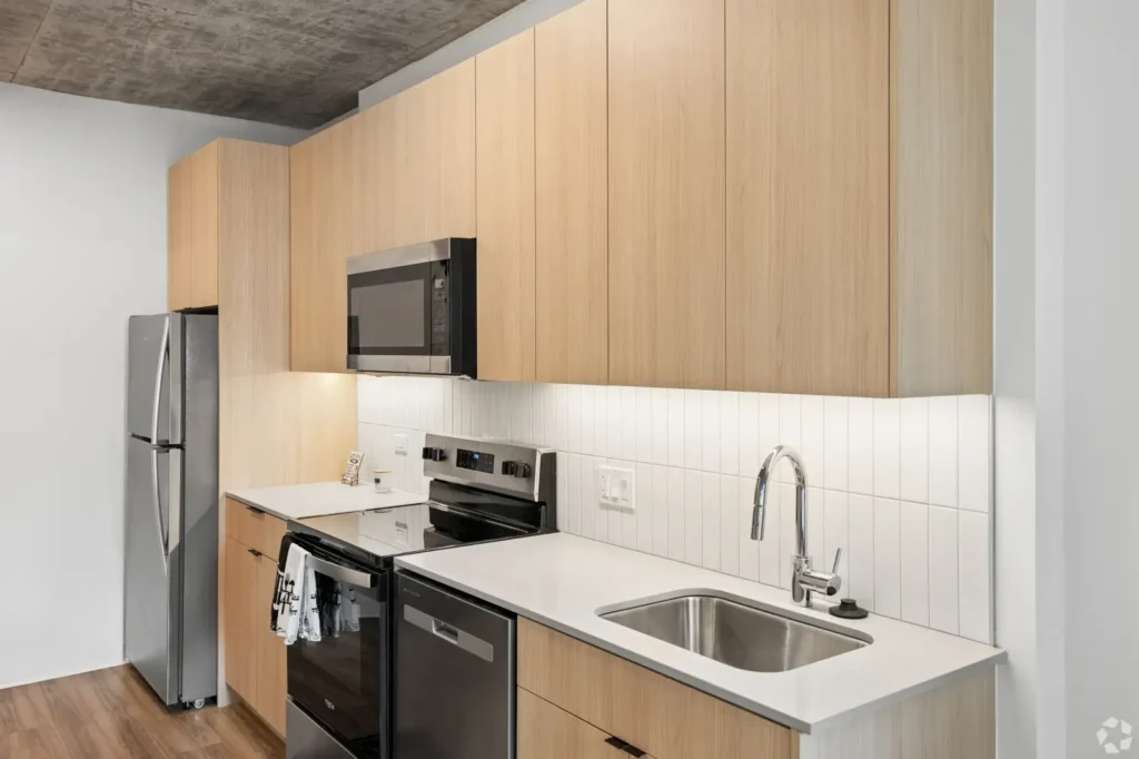Studio kitchen with a marble waterfall island, wood cabinetry, stainless steel appliances, and pendant lights.