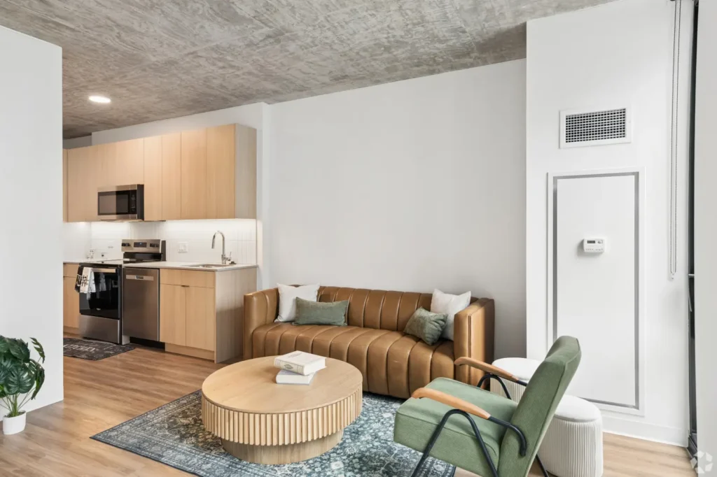 Studio living area with a sofa, coffee table, dining table, TV, and large windows with city views.